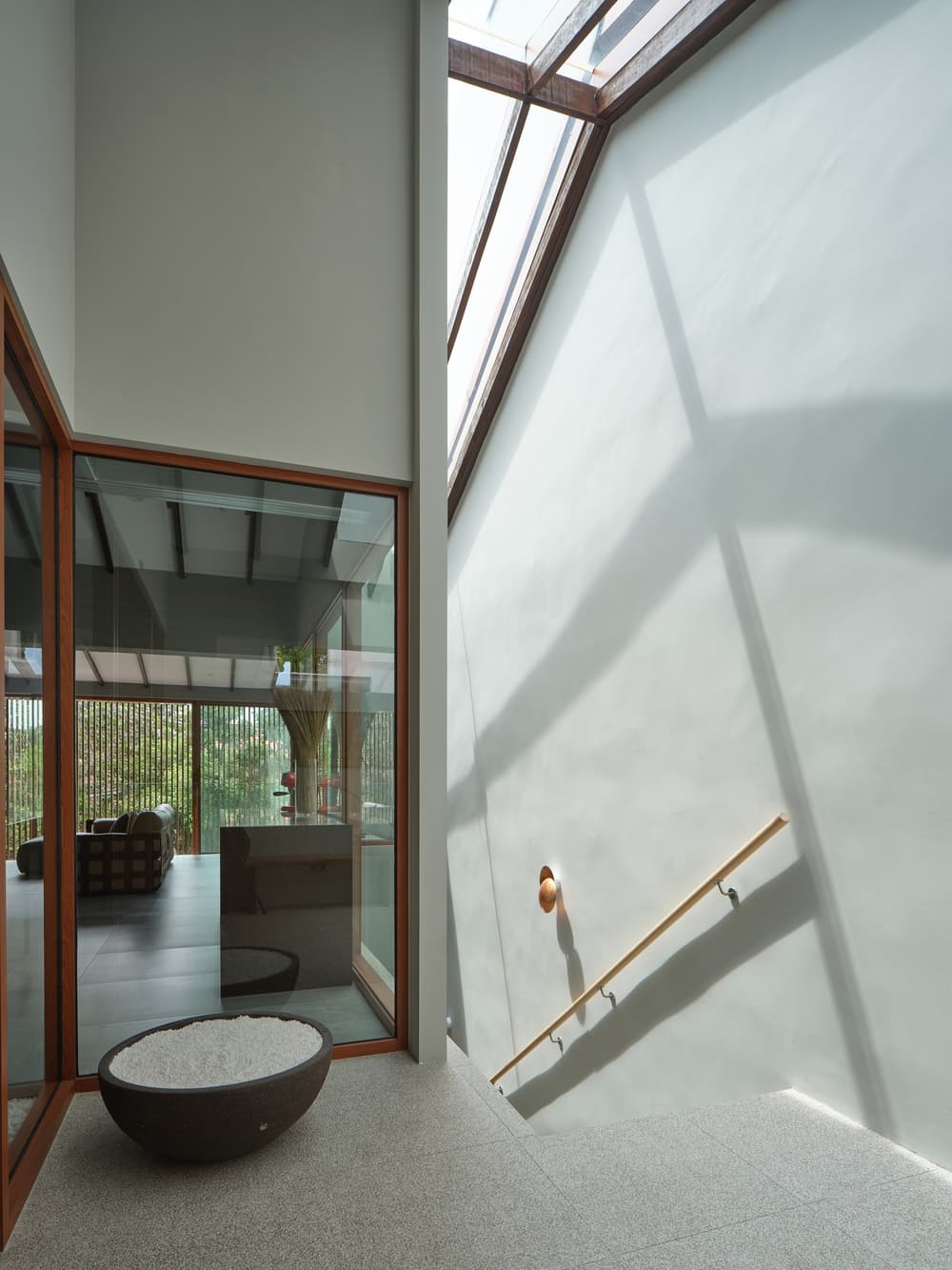 Skylight shadow falling across the stairwell wall above a stone bowl at A Sensory House, a luxury landed house interior in Singapore by K2SD Group
