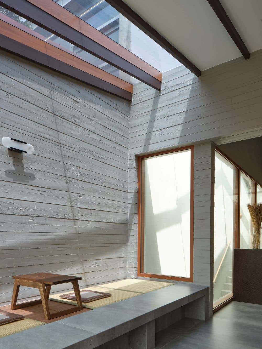 Light across the board marked concrete wall above the tatami platform at A Sensory House, a luxury landed house interior in Singapore by K2SD Group