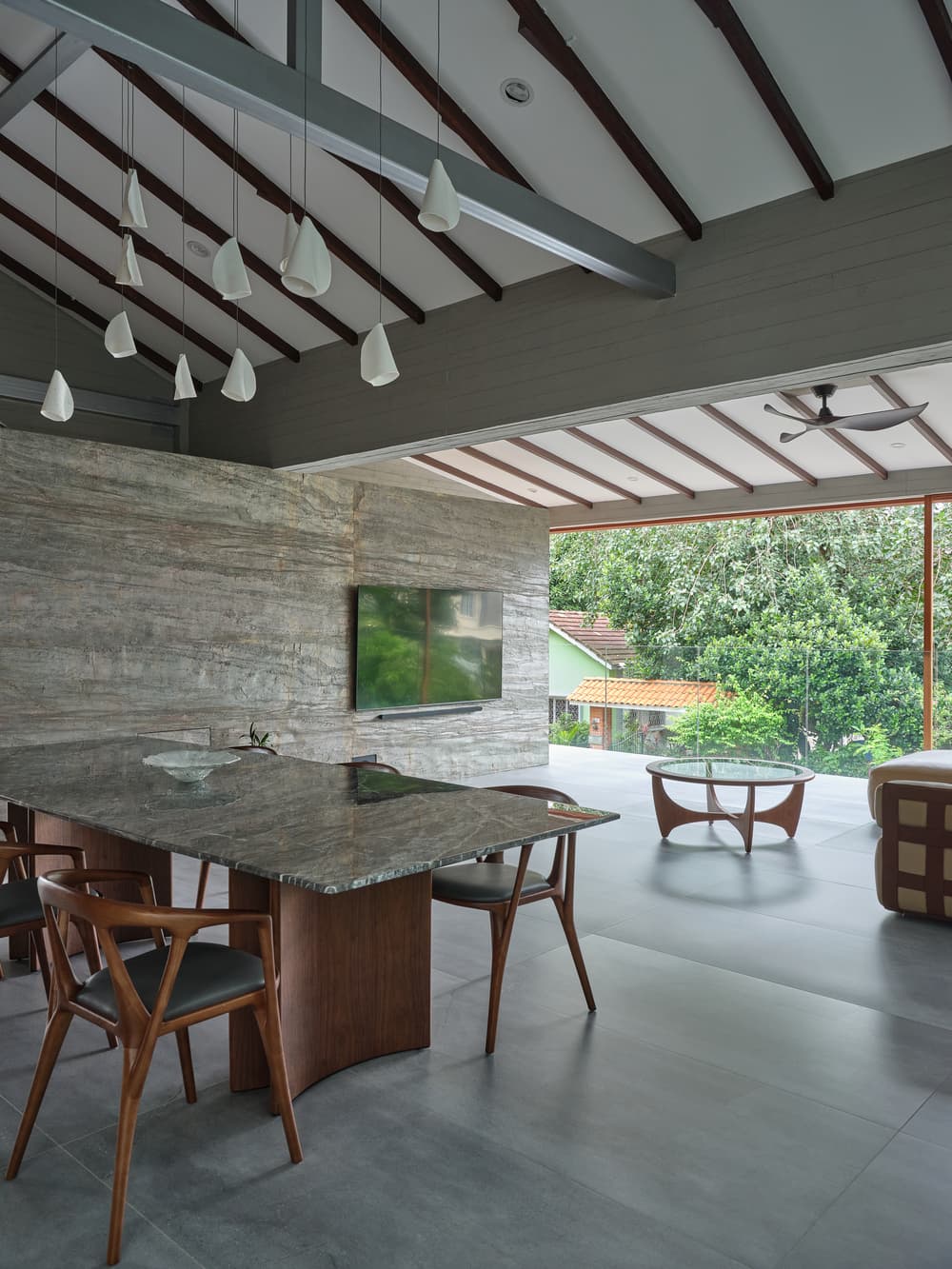 The dining table beneath the pitched timber roof at A Sensory House, open to the garden, a luxury landed house interior in Singapore by K2SD Group