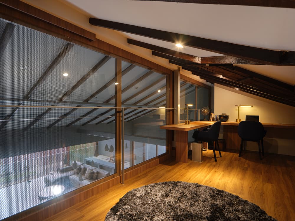 The loft study under the roof beams, looking down through glass to the living hall at A Sensory House, a luxury landed house interior in Singapore by K2SD Group