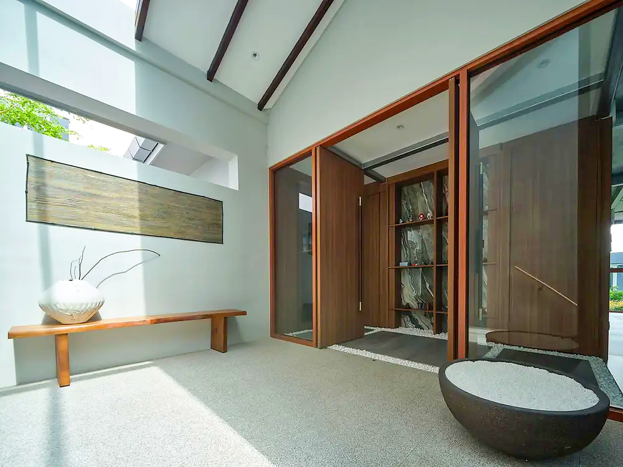 A long mounted panel above the timber entrance bench and its white vessel, beside a stone bowl of gravel, at A Sensory House, a luxury landed house interior in Singapore by K2SD Group