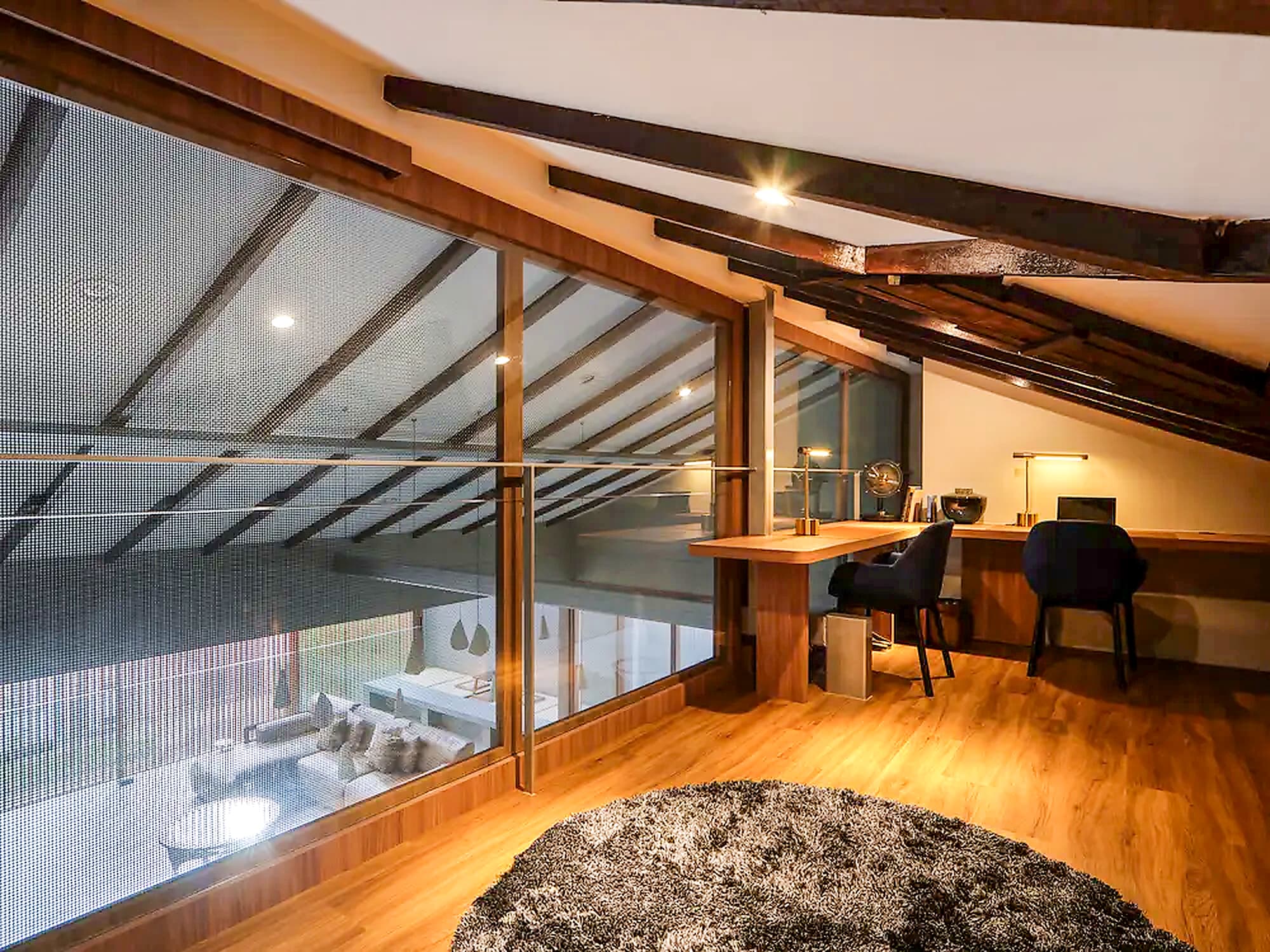 The loft study under the roof beams, looking down through glass to the living hall at A Sensory House, a luxury landed house interior in Singapore by K2SD Group