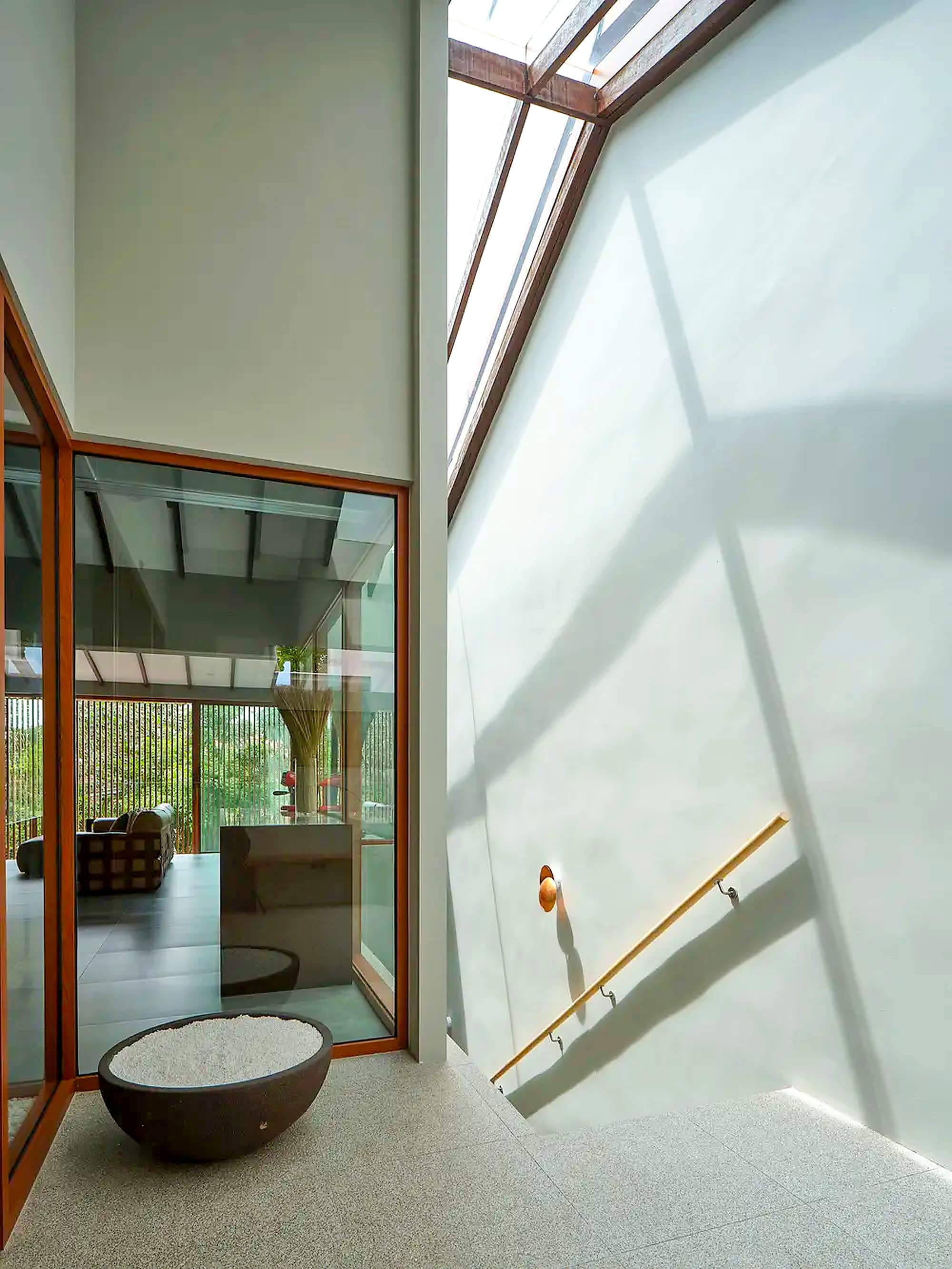 Skylight shadow falling across the stairwell wall above a stone bowl at A Sensory House, a luxury landed house interior in Singapore by K2SD Group
