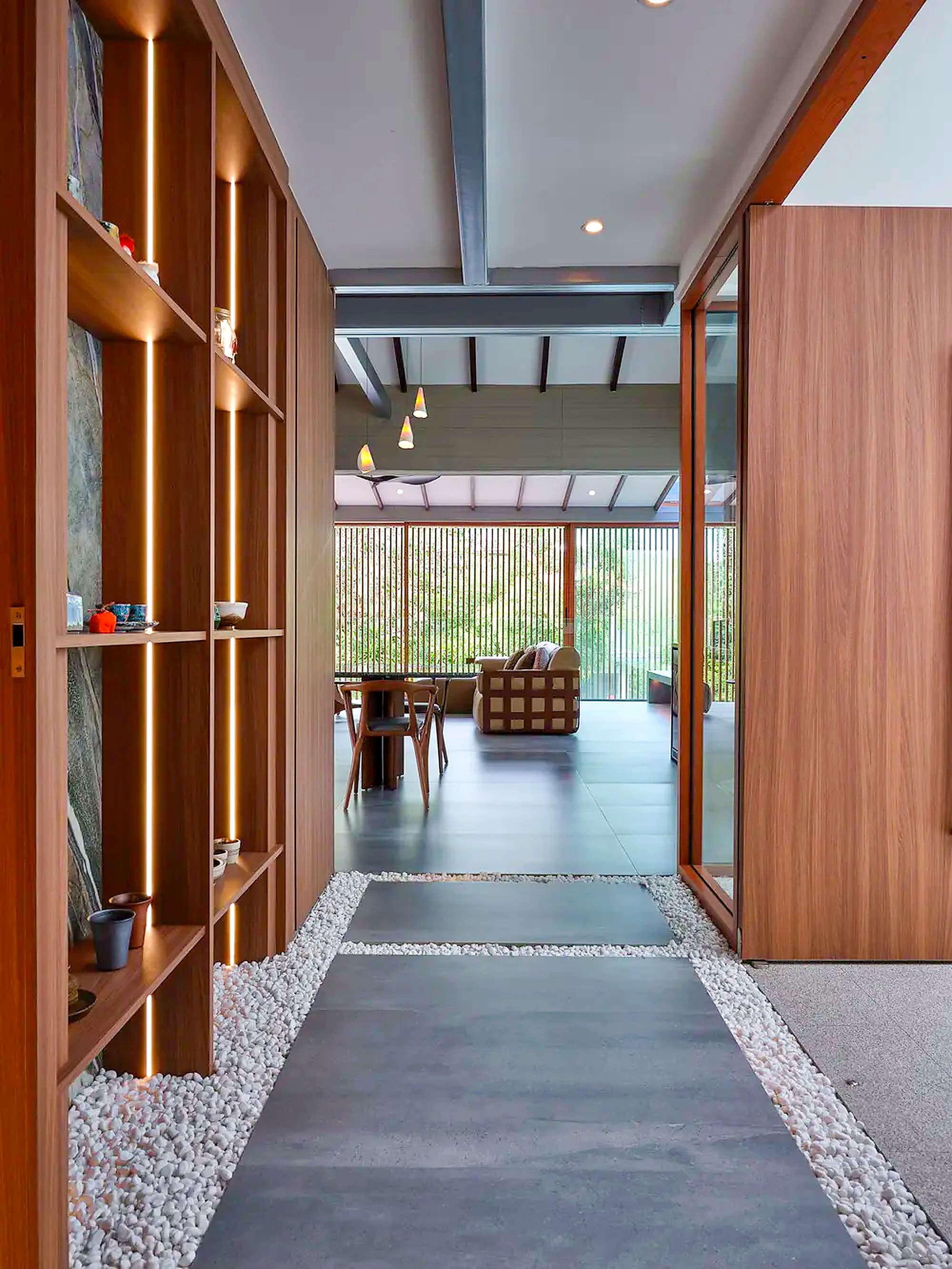 The stone path between beds of white pebbles, past a lit timber shelf of ceramics to the dining room, at A Sensory House, a luxury landed house interior in Singapore by K2SD Group